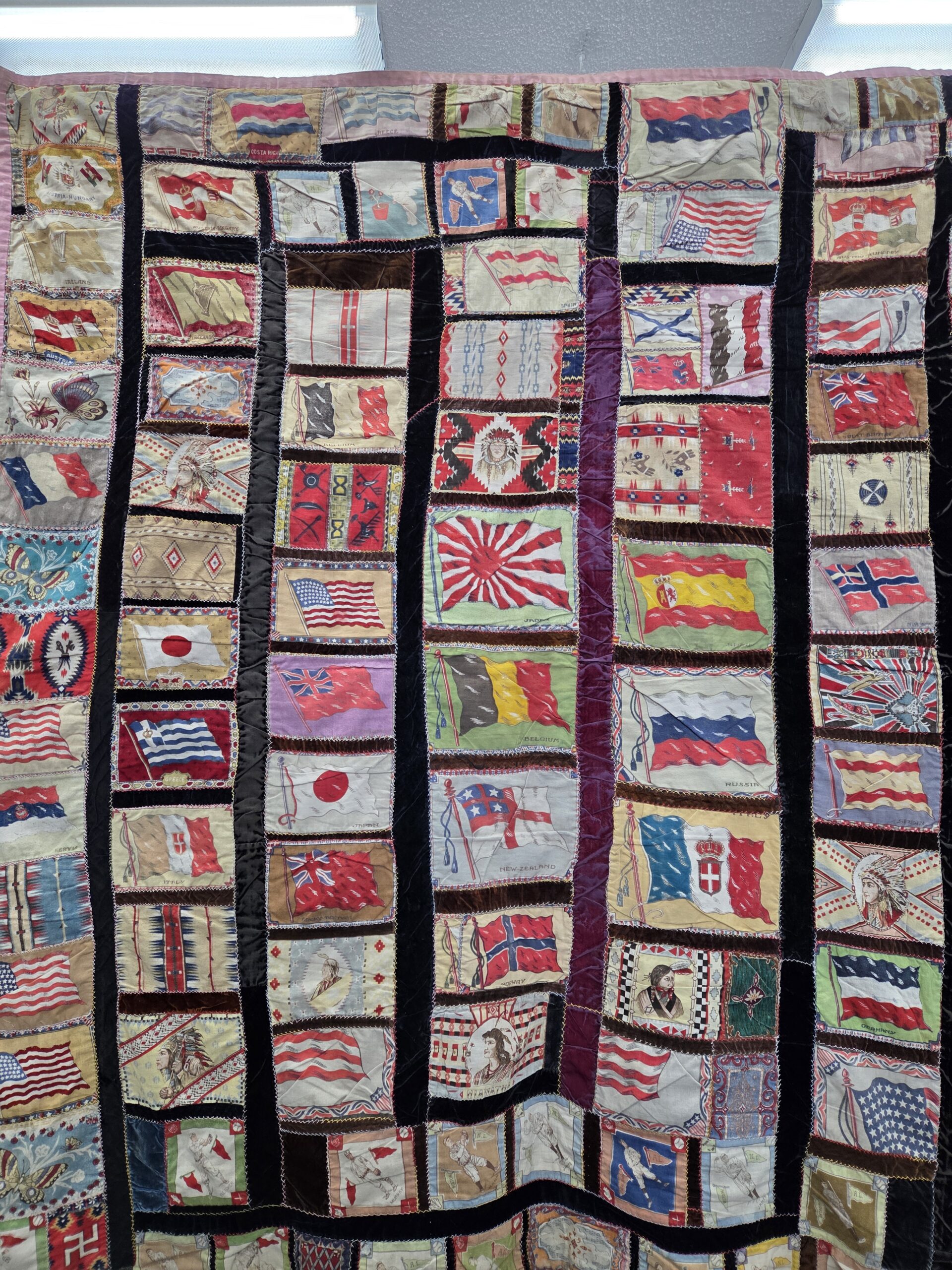 Tobacco Premium Quilt with printed panels of national flags, figures, and decorative motifs separated by dark fabric strips.
