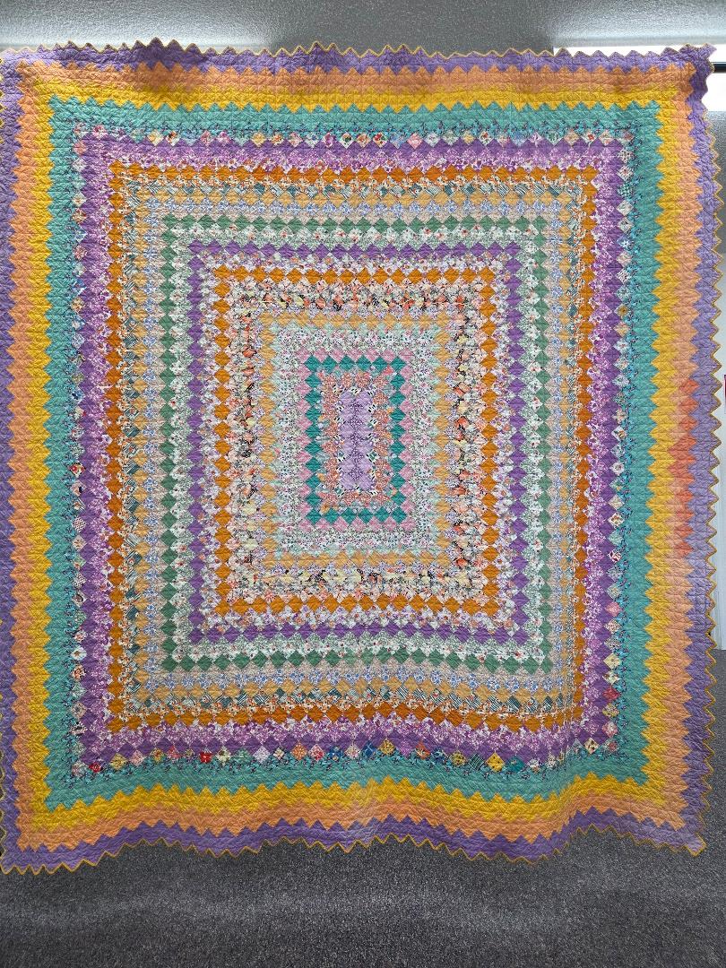 Trip Around the World quilt with concentric rows of small fabric squares in purple, turquoise, yellow, and floral prints.
